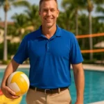 Coordinador de deportes en resort sosteniendo balón frente a piscina con red de voleibol